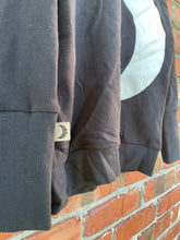 Load image into Gallery viewer, Close-up of pale crescent moon appliqué with stitched edging on black fabric.