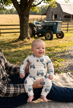 Load image into Gallery viewer, Baby on a farm with a blue Ford tractor in the background